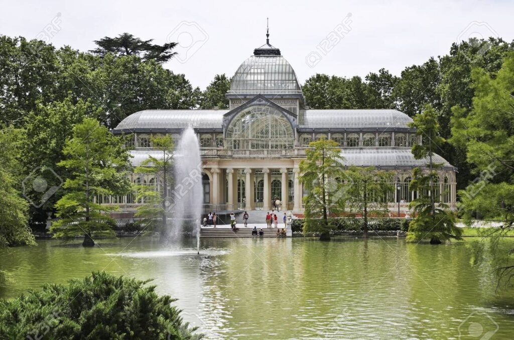 Crystal Palace in Retiro Park, Madrid, Spain, with a fountain and lake surrounded by trees on a bright day. Madrid Winter Travel Guide 2025: Best Things to Do, See & Eat.