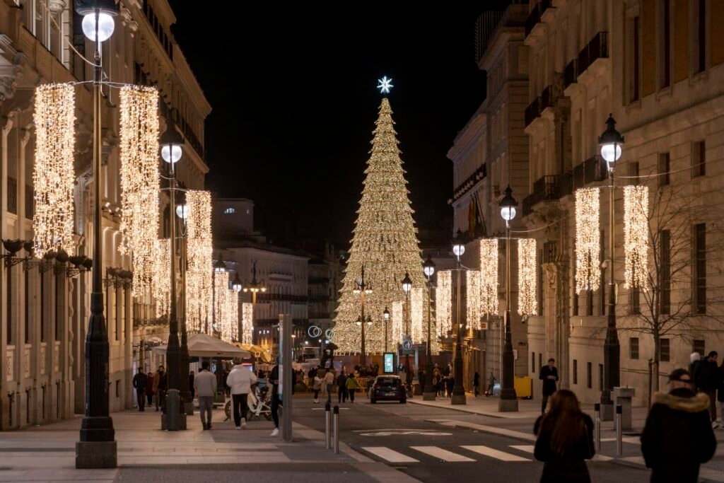 Christmas lights and a giant illuminated tree at Puerta del Sol in Madrid, Spain, during the holiday season at night. Madrid Winter Travel Guide 2025: Best Things to Do, See & Eat.